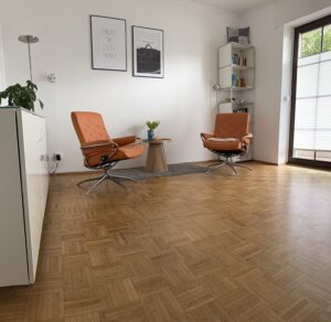 Heller Therapieraum mit zwei orangefarbenen Sesseln und Glasfront in der Praxis Michael Backes in Ratingen.